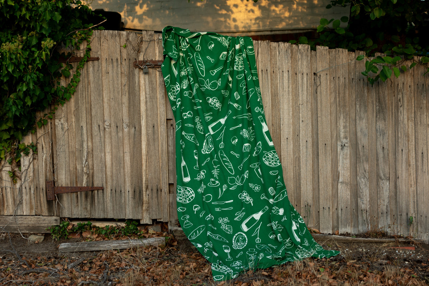 The "Green Feast" tablecloth is displayed in a lush outdoor setting, highlighting its striking green color and clean, hand-drawn patterns that celebrate simplicity and sophistication.