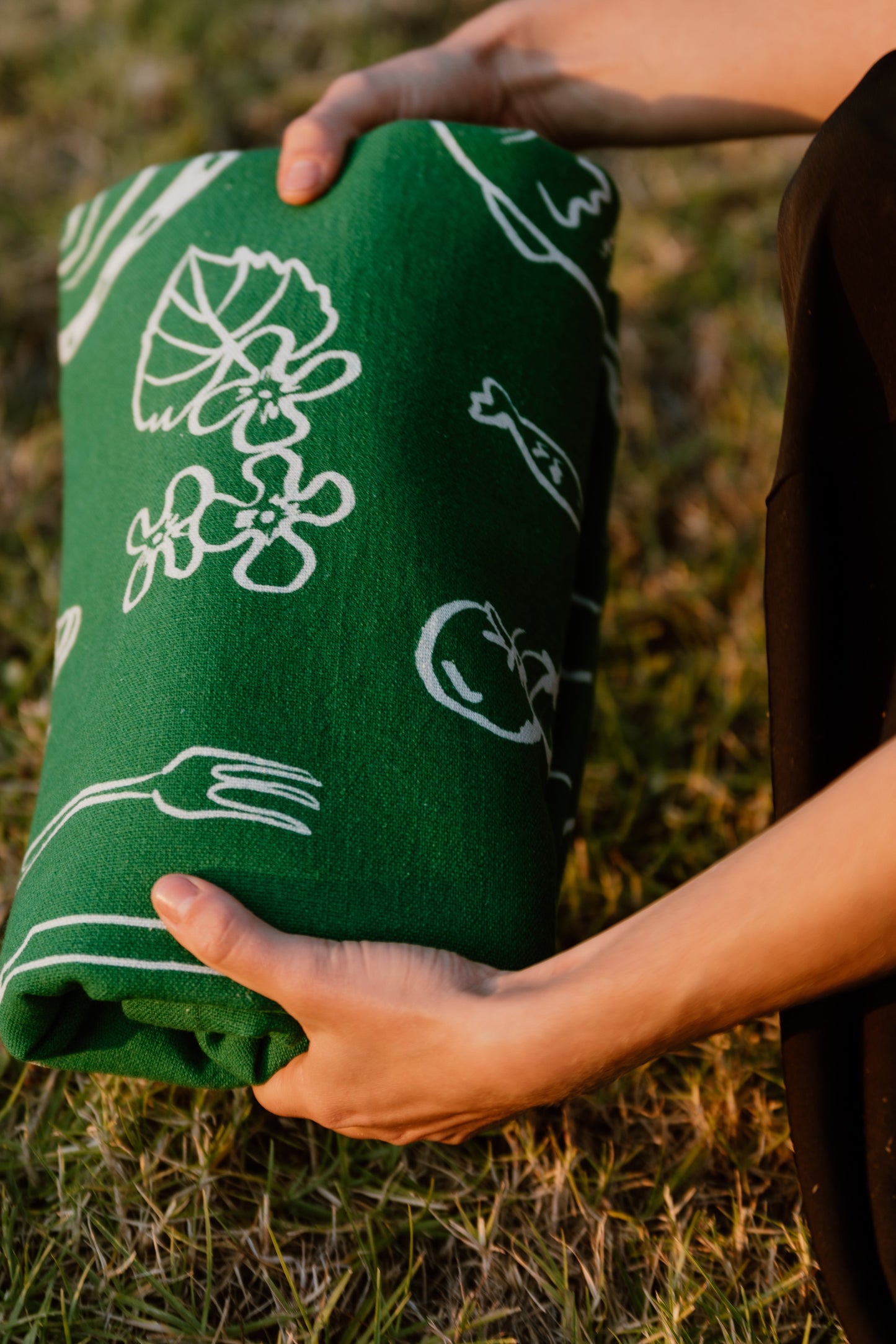 A close-up of hands holding the folded Green Feast tablecloth, emphasizing its soft texture, handmade quality, and the subtle, elegant design inspired by Greece.