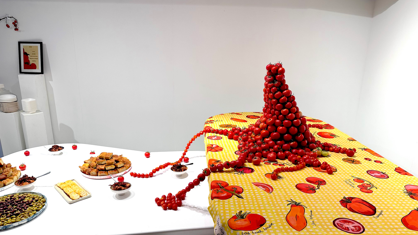 Tower of cherry tomatoes arranged playfully on a tomato-themed tablecloth. Beads of tomatoes stretch out across the table like spaghetti arms.