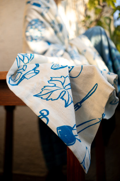 Corner of a Grecian-style blue and white tablecloth elegantly hanging over the edge of a wooden table with lemons nearby