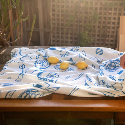 White and blue printed tablecloth draped over a wooden bench with lemons, capturing the soft outdoor lighting and surrounding greenery