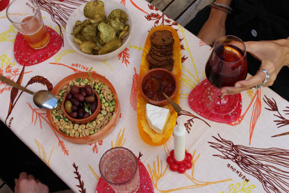 A vibrant table setting with snacks and drinks atop the GRANO tablecloth, showcasing the warmth and vibrancy of the Australian landscape. The rich orange and yellow shades of the tablecloth, inspired by the native grains and the outback, create a lively backdrop for olives, cheese, crackers, and a glass of red wine.