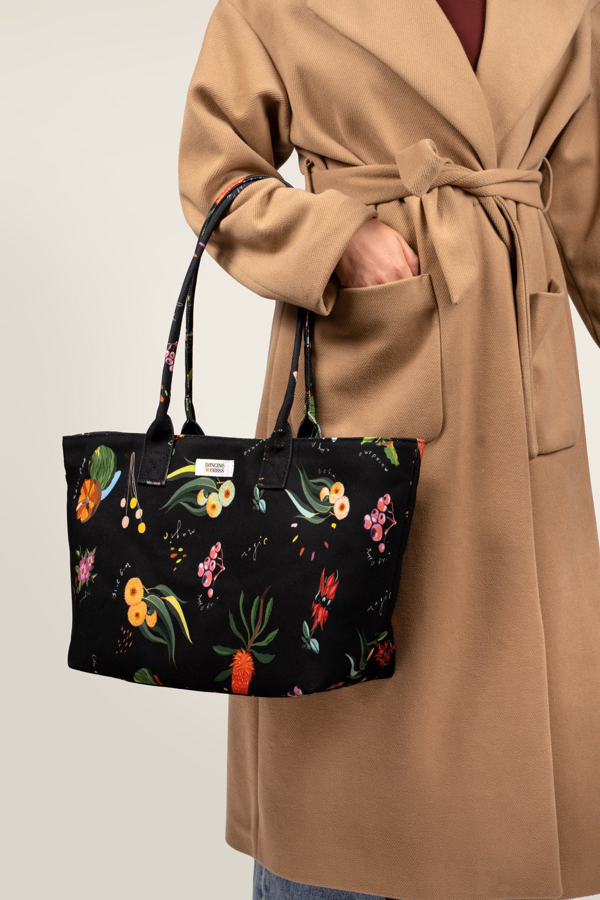 The Dark Flora Dancing Grass bag held in hand, styled with a camel coat