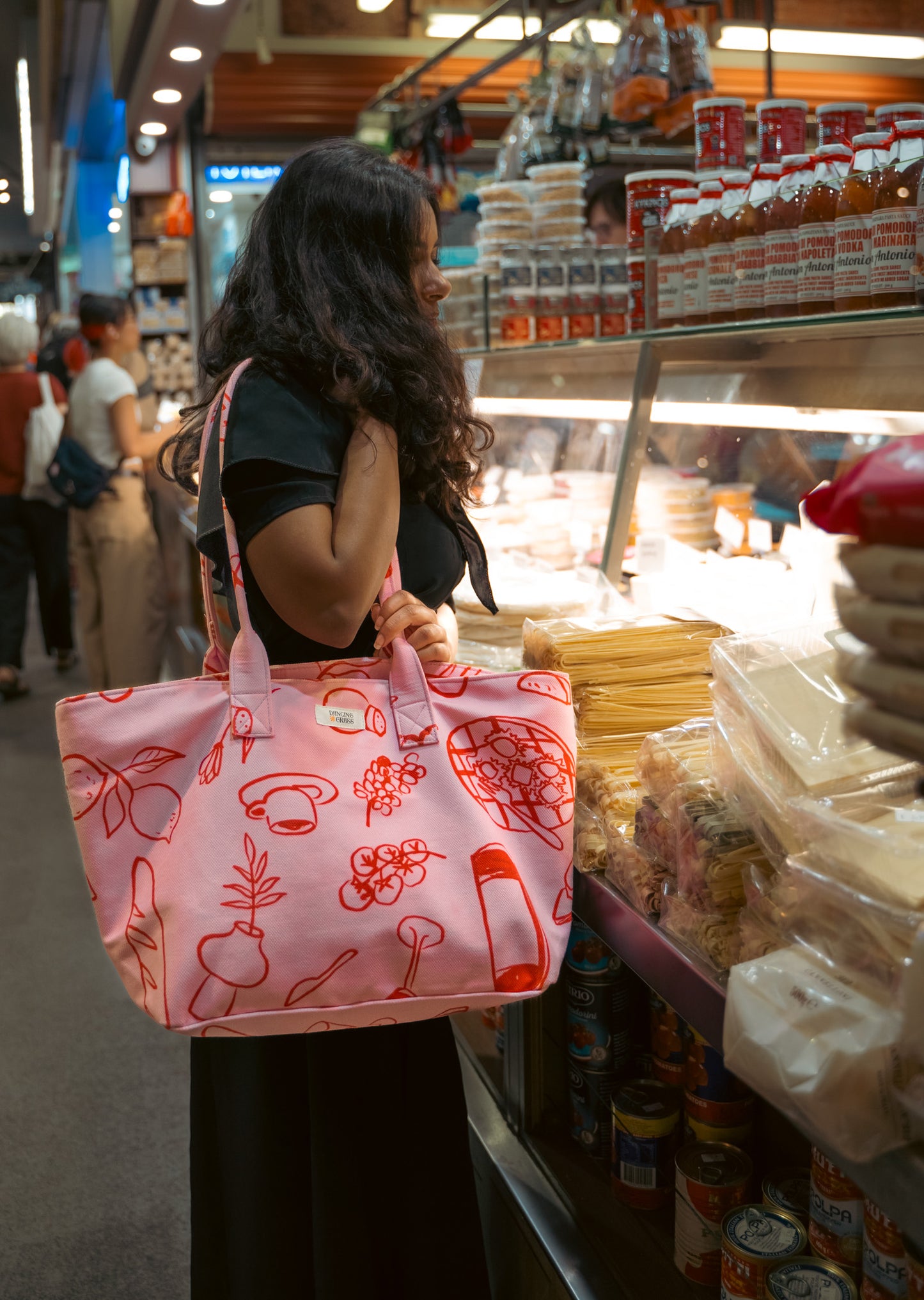 Pink canvas tote bag with red illustrated print carried while shopping at an Italian grocery store